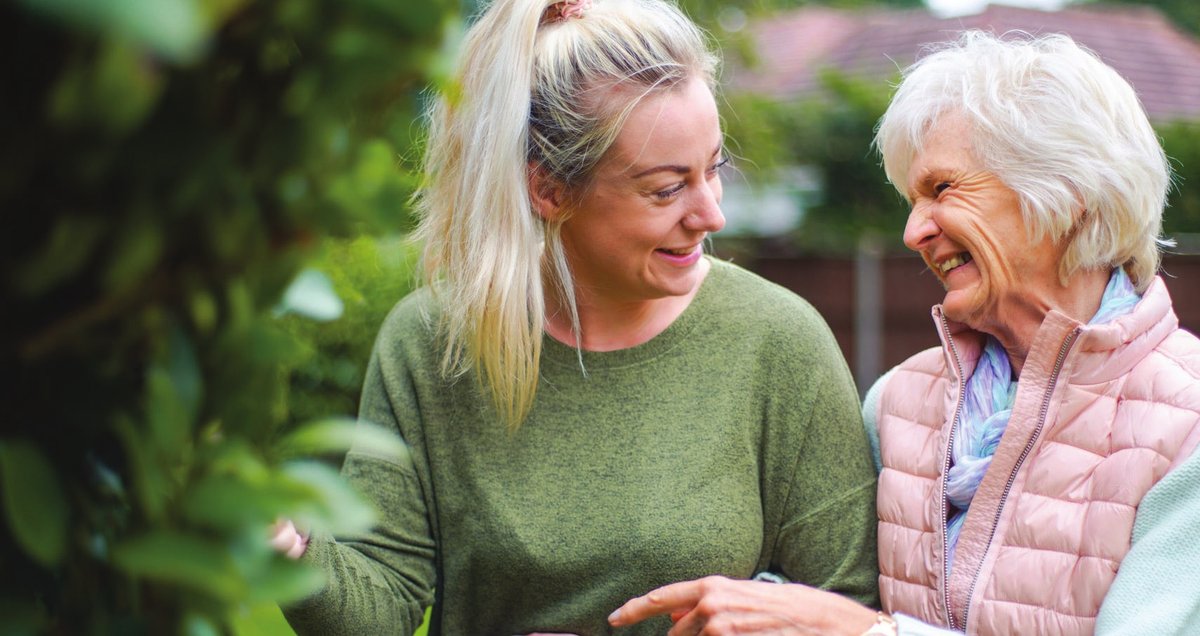 A young carer and an older woman laughing together in a garden