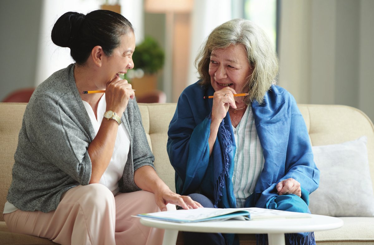 Two women laughing together over a notebook on a sofa
